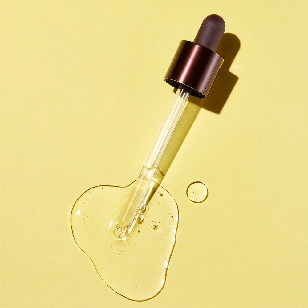 Dropper with clear brightening serum on bright yellow background highlighting texture and glow
