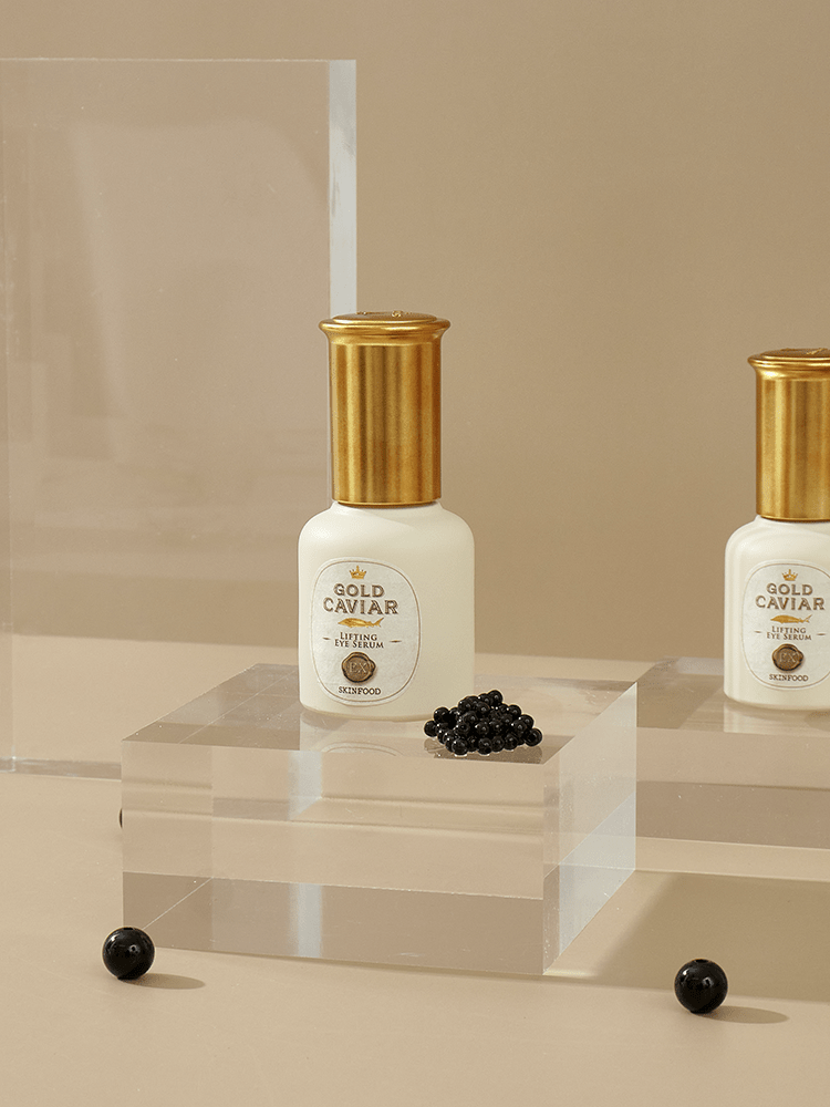 Bottle of firming eye serum with gold cap and black caviar beads on clear acrylic display against beige background