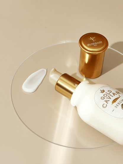 White serum bottle with gold pump and cap next to a cream swatch on clear round tray, promoting firmness boost benefits