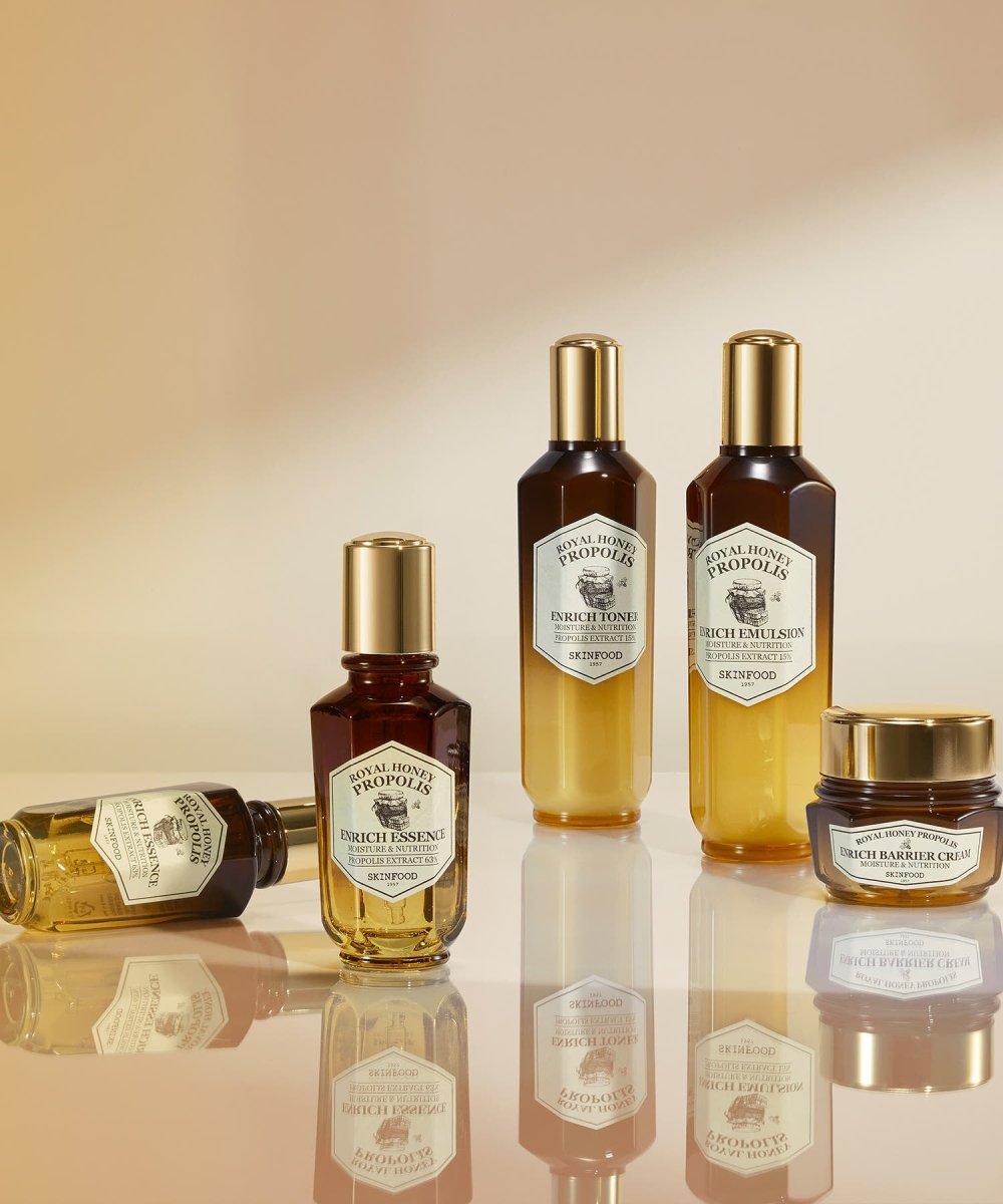 Collection of skincare bottles and jar with gold caps featuring rich honey propolis essence and barrier cream in amber and yellow gradient tones