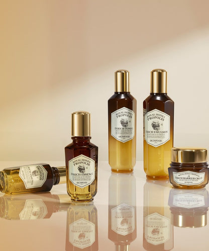 Collection of skincare bottles and jar with gold caps featuring rich honey propolis essence and barrier cream in amber and yellow gradient tones