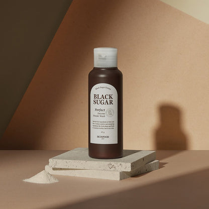 Dark brown bottle of gentle exfoliating enzyme powder wash beside a small heap of powder on beige textured slabs