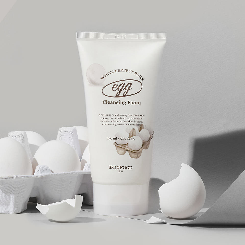 Tube of pore-cleansing foam with egg white graphic beside whole and cracked white eggs on gray background
