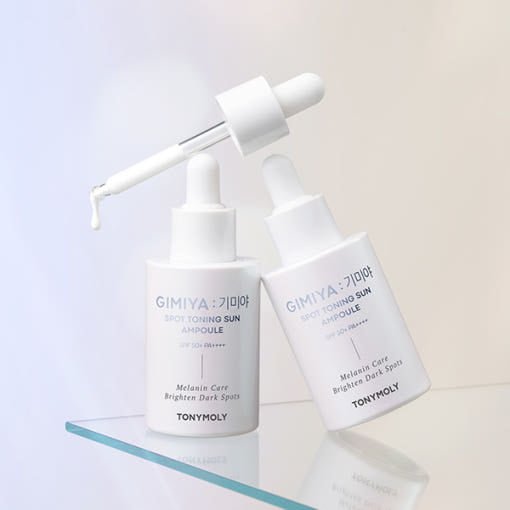 Two white dropper bottles of sun ampoule with clear liquid on reflective glass surface and soft background
