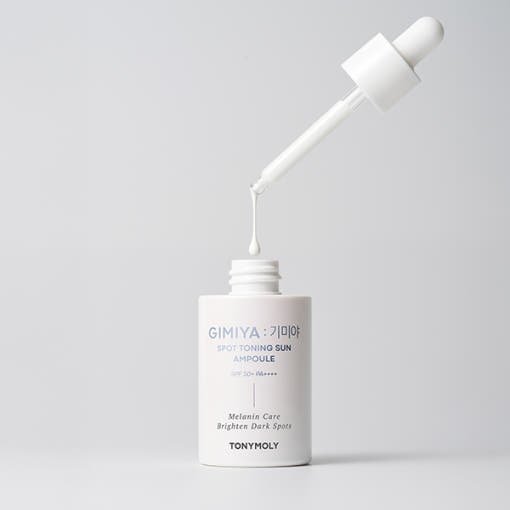 White dropper bottle of toning sun ampoule with dropper applicator releasing liquid above the open neck