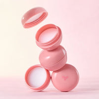 Stack of pastel pink round containers with white moisturizing lip balm inside against soft gradient background