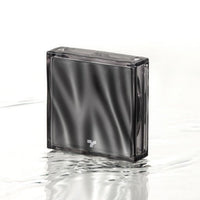 Sleek black compact cushion case with reflective surface standing on rippled water background