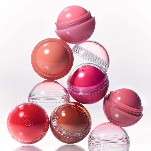 Seven spherical cheek tint containers in various pink and coral shades stacked on a reflective white surface