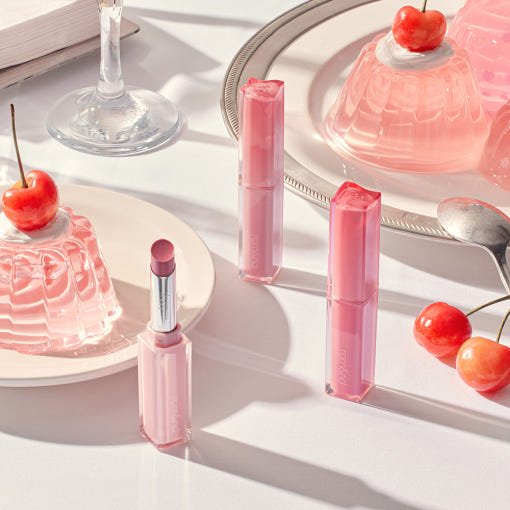 Three pink tinted sticks with transparent caps displayed alongside pink gelatin desserts topped with cherries on white plates