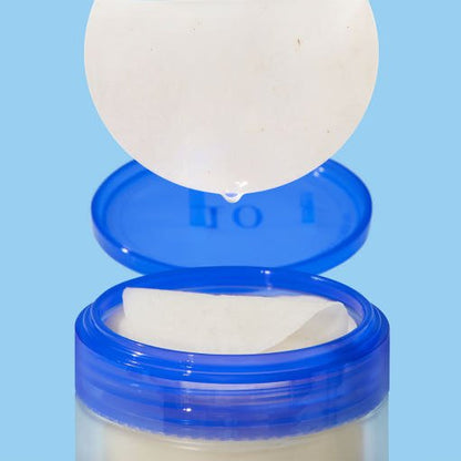 Open blue jar with round toner pad dripping liquid above, showcasing hydration boost skincare product