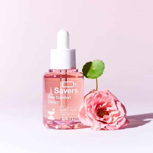 Clear glass dropper bottle of soothing pink serum next to a delicate pink flower on pale pink background