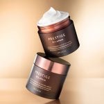 Two dark amber jars of firming glow sleeping mask with pale pink cream visible in the open top jar on soft beige background