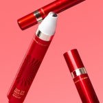 Red tube of eye serum with silver rollerball applicator for revitalizing skin care on pink background
