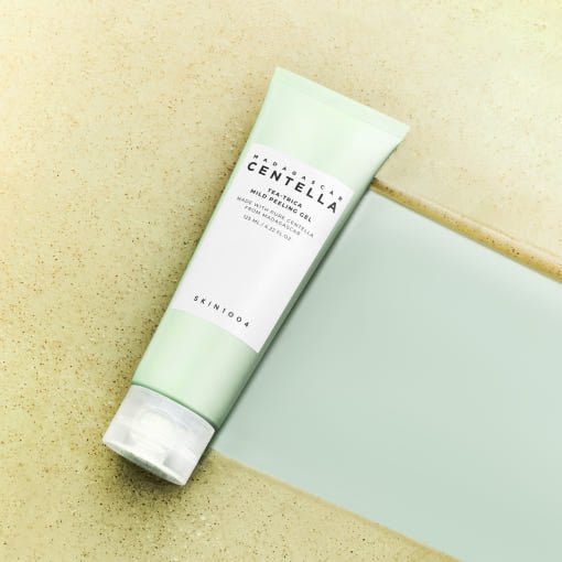 Tube of mild peeling gel with soft green packaging lying on textured beige and smooth blue surfaces
