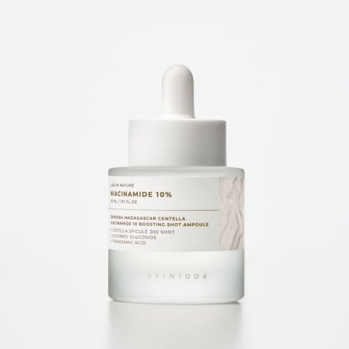 Frosted glass dropper bottle with white label featuring niacinamide 10% brightening serum on plain background
