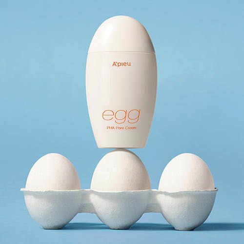 A'pieu Egg PHA Pore Cream 65g bottle balanced on three white eggs in textured carton against blue background