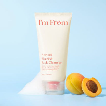 Tube of gentle exfoliating apricot sherbet cleanser with foam and fresh apricots on pale blue background