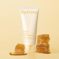 Cream-colored tube of cleanser with honeycomb pieces and honey drips on soft beige background