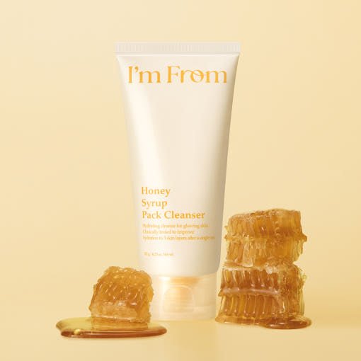 Tube of cleanser with honey syrup graphic, surrounded by dripping honeycomb on beige background