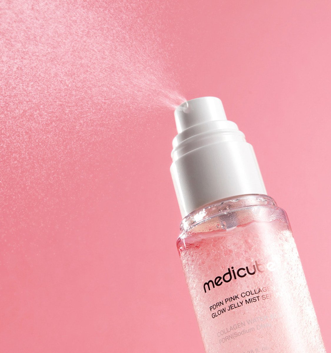 medicube PDRN PINK COLLAGEN GLOW JELLY MIST SERUM 100ml spraying fine mist for radiant glow benefits on pink background
