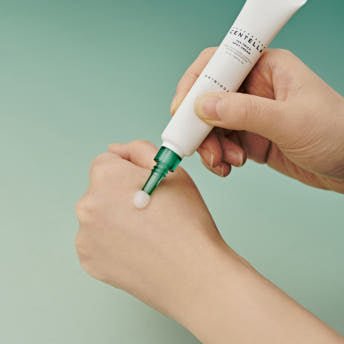 Hand applying smooth white cream from a white tube with green nozzle, highlighting calming spot treatment benefits