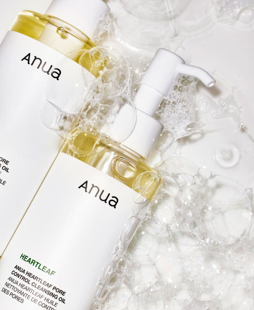 Two clear pump bottles with pale yellow cleansing oil surrounded by frothy bubbles on white surface