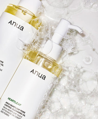 Two clear pump bottles with pale yellow cleansing oil surrounded by frothy bubbles on white surface