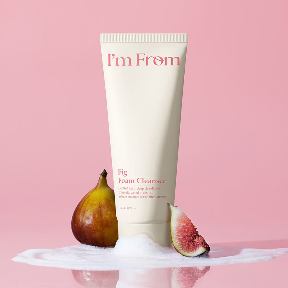 Tube of gentle fig foam cleanser with fresh fig fruit and creamy lather on a soft pink background